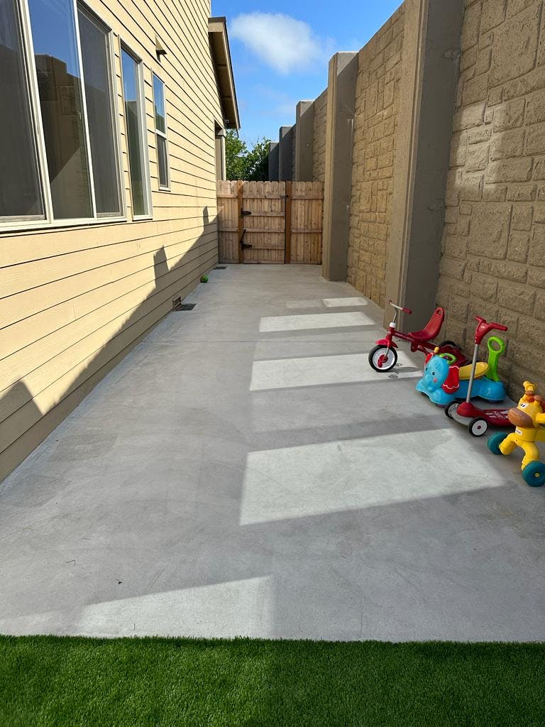 Side yard with concrete path, wooden fence, and children's toys