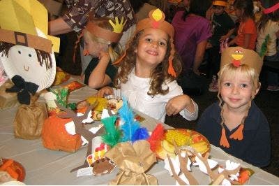 Two children wearing turkey hats at a table with crafts