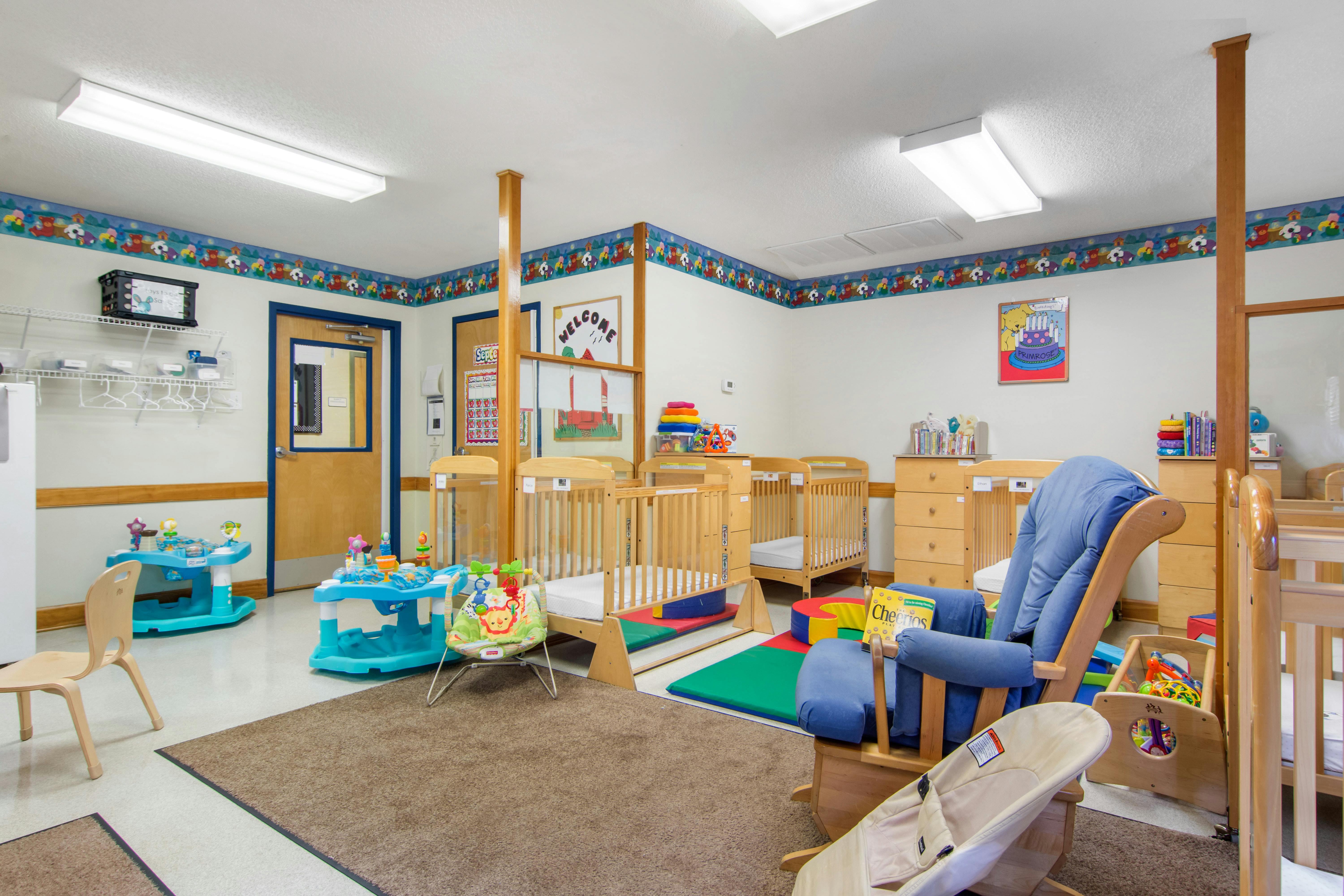 Cribs, play areas, and a blue rocking chair in a bright infant room