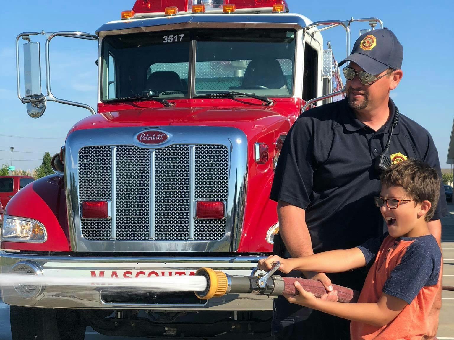 Person and child holding a fire hose in front of a fire truck