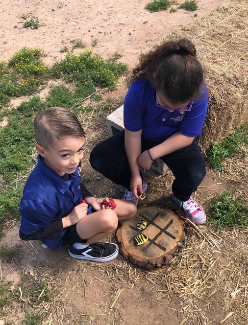 Two children playing tic-tac-toe on a tree stump