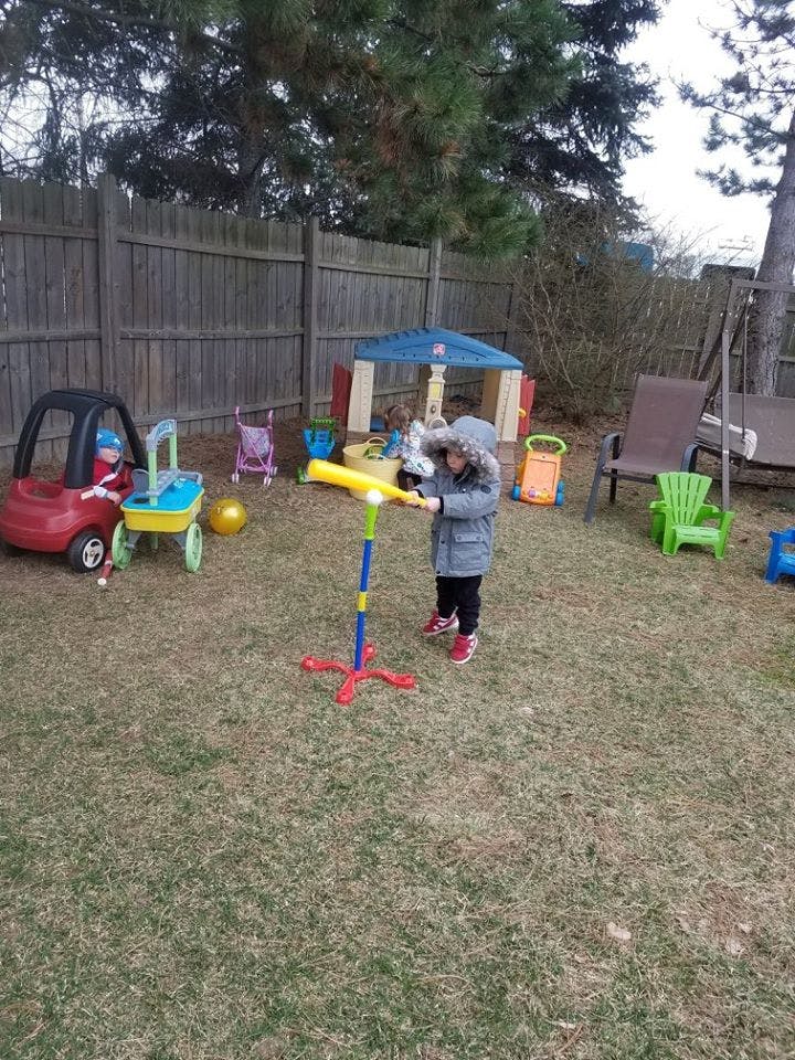 Child playing with a T-ball set in a yard