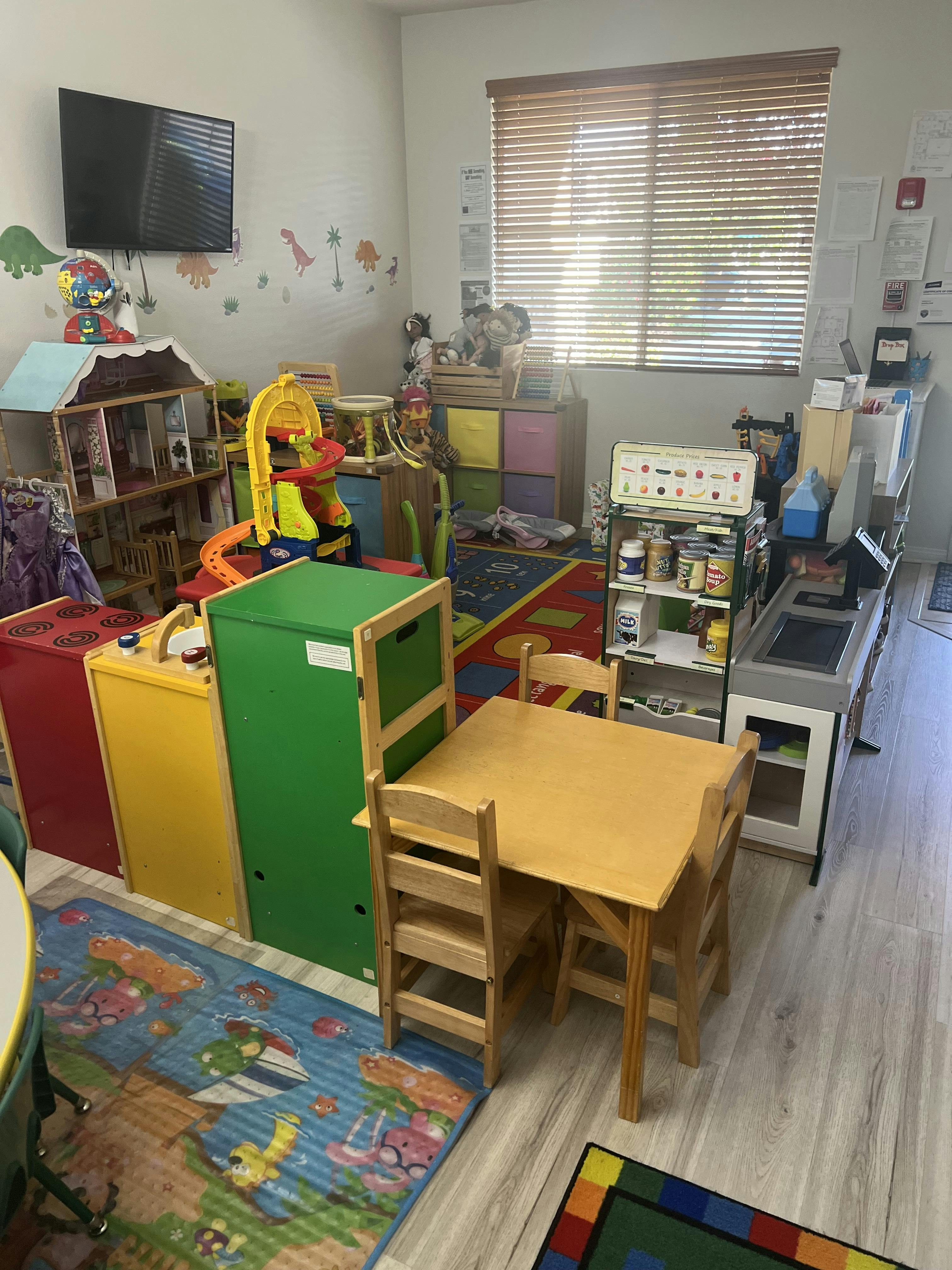 A room in a childcare center with toys, a play kitchen, and a small table with chairs