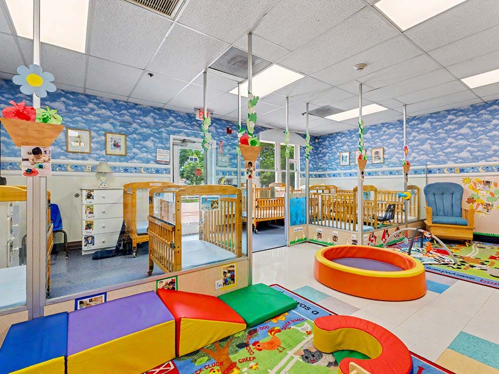 A colorful childcare room with several wooden cribs, playmats, and soft play equipment