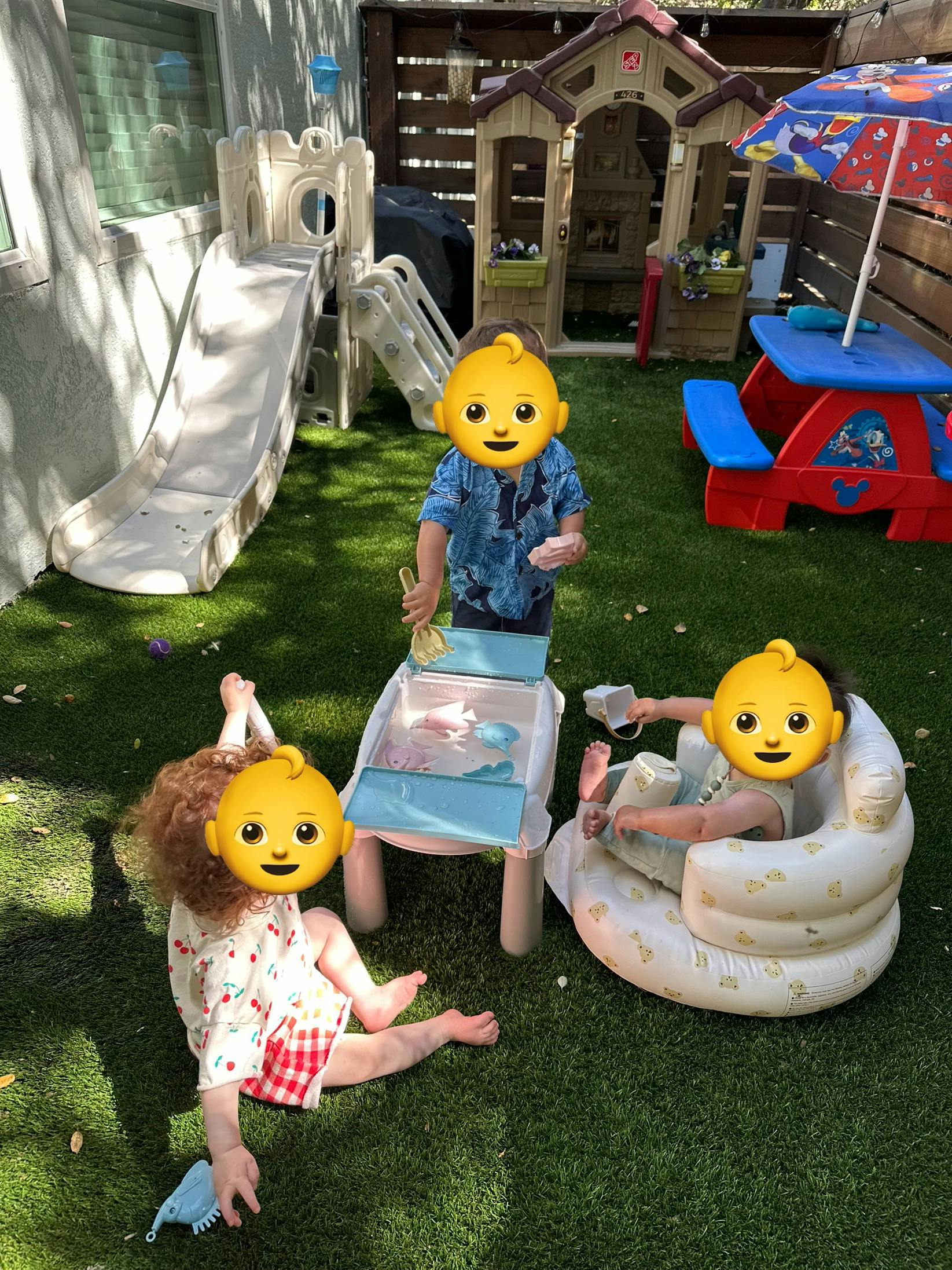 Three children playing outdoors with toys and a water table