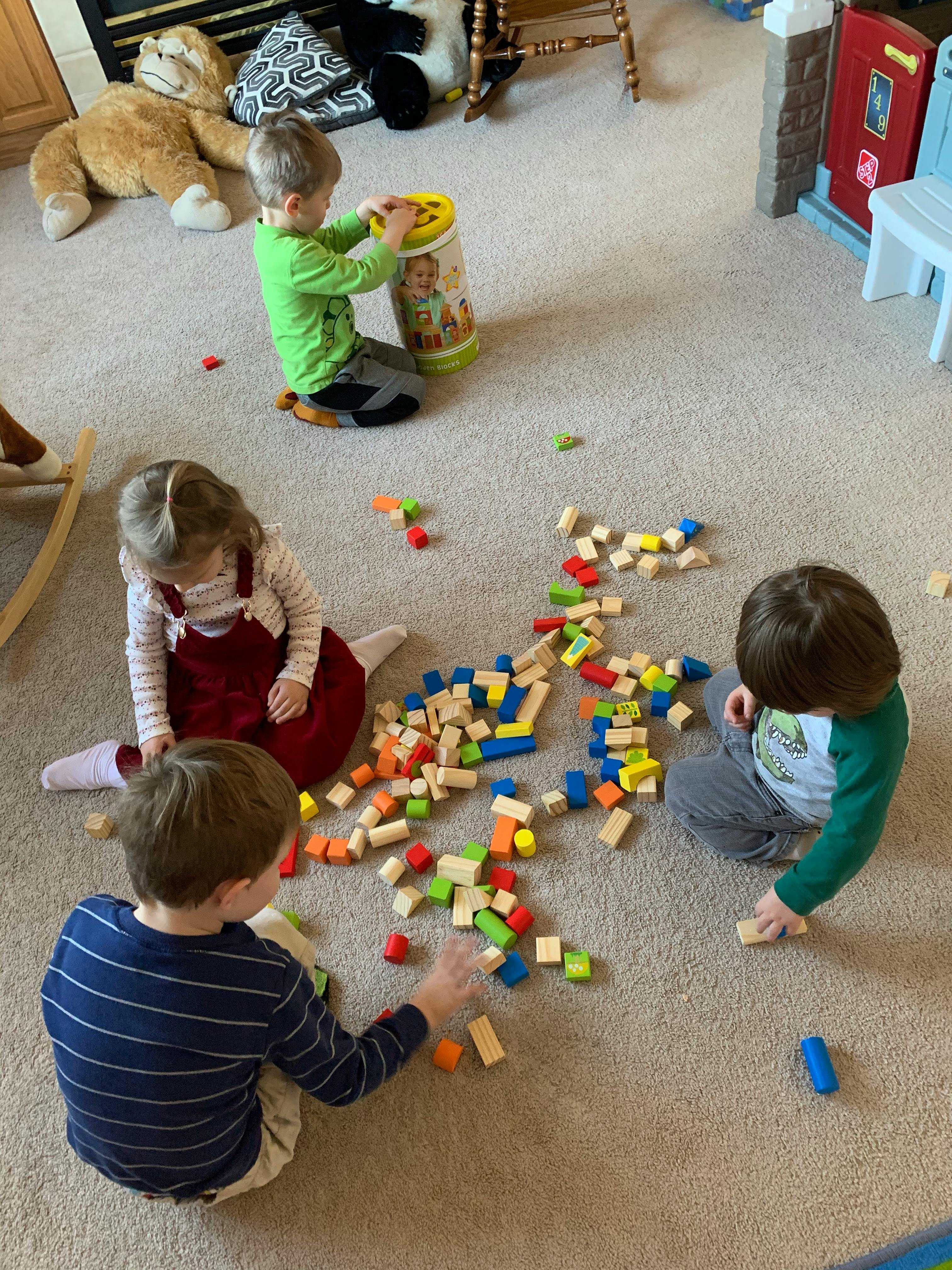 Three children playing with colorful building blocks on a carpet