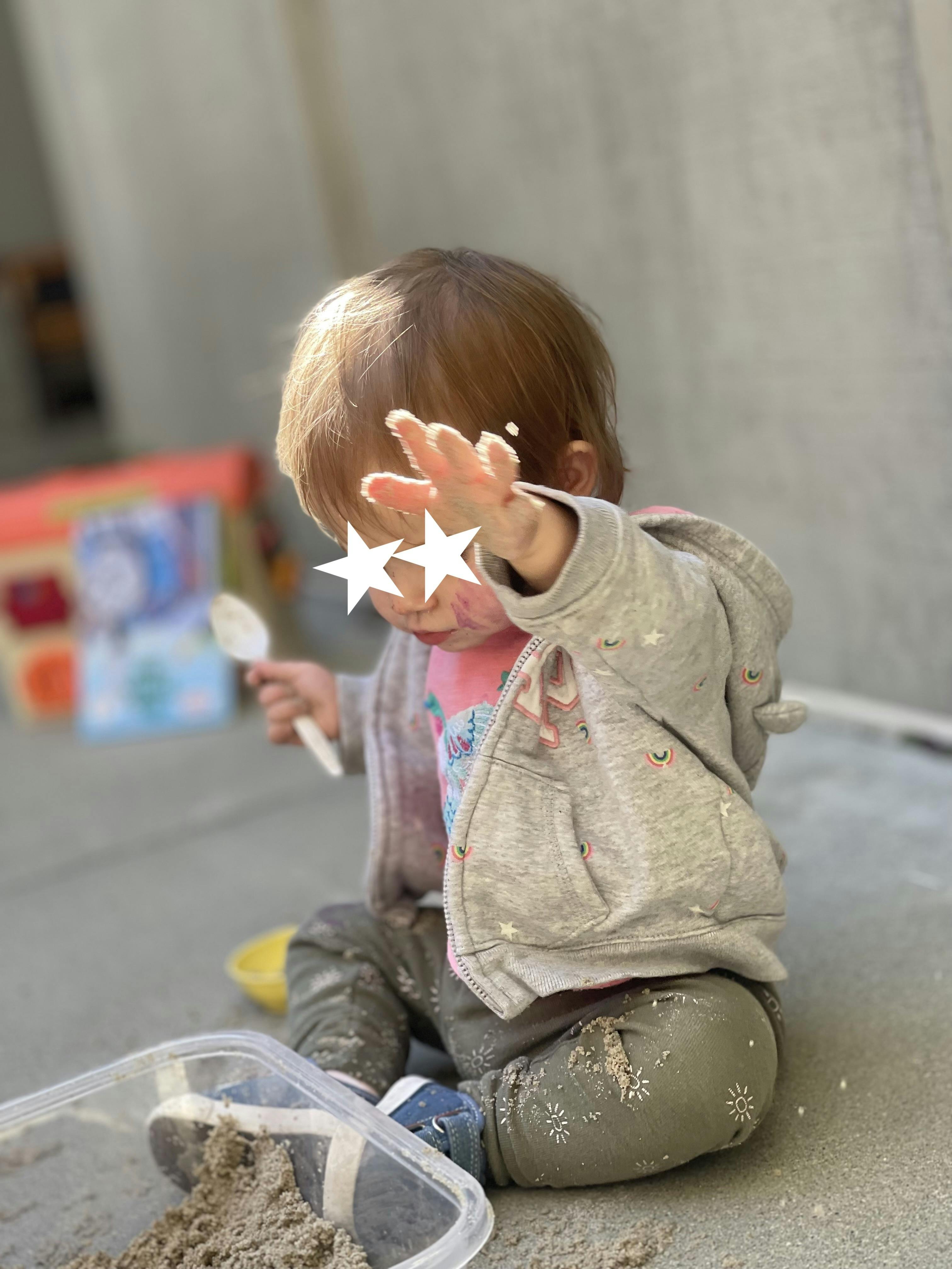 Child playing in sand with a spoon