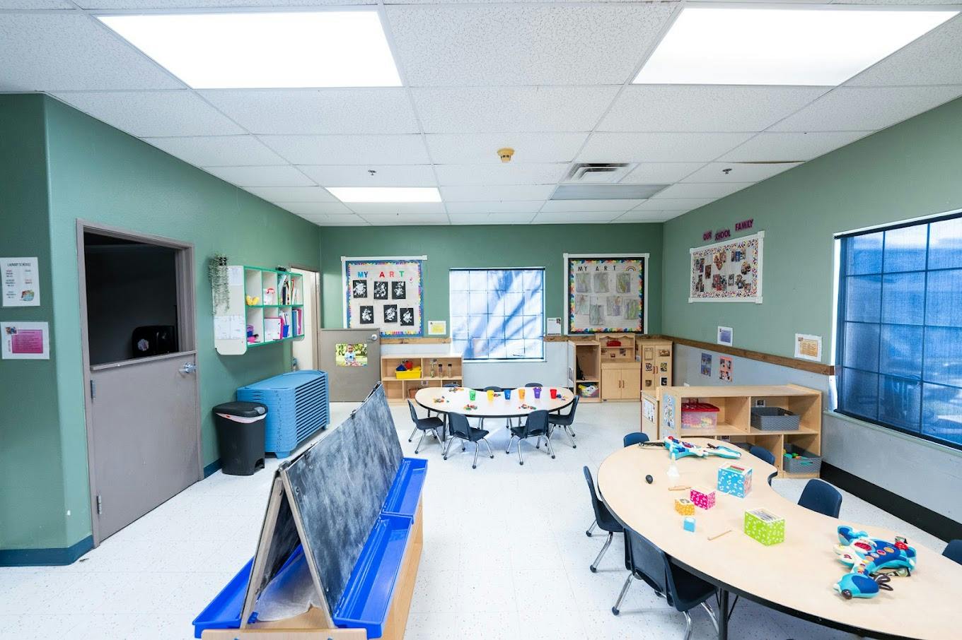 Empty preschool classroom with tables, chairs, and learning materials