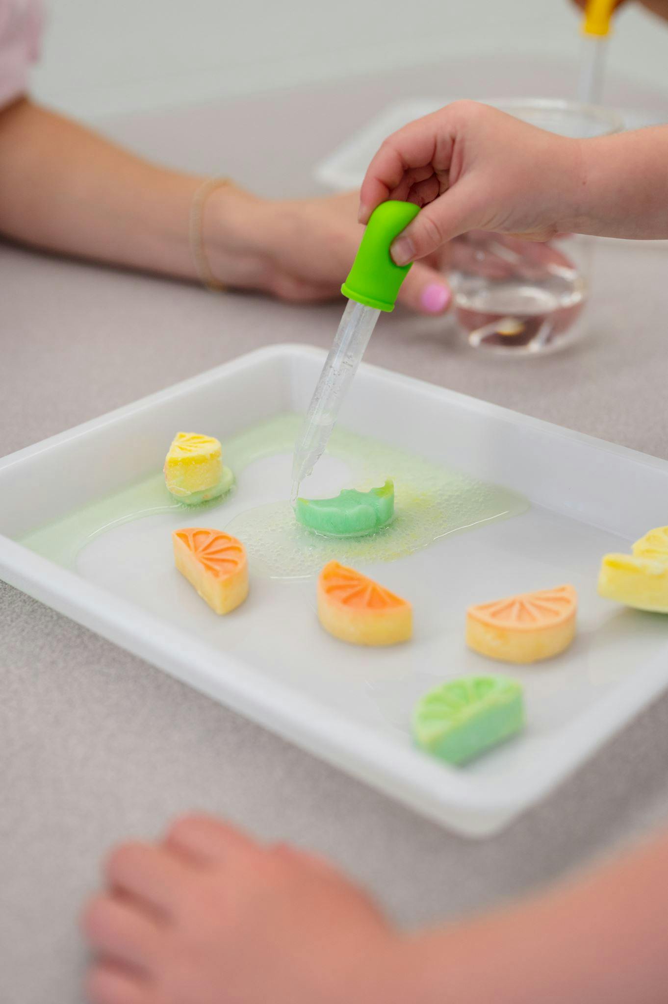 Child using a dropper to add liquid to small fruit-shaped pieces on a tray