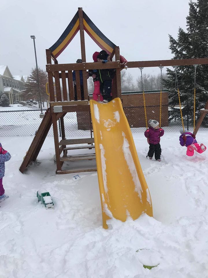 Children playing on a snow-covered playground structure with a slide and swings