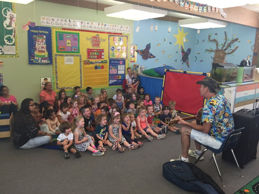 Person playing guitar for a group of children and adults in a classroom