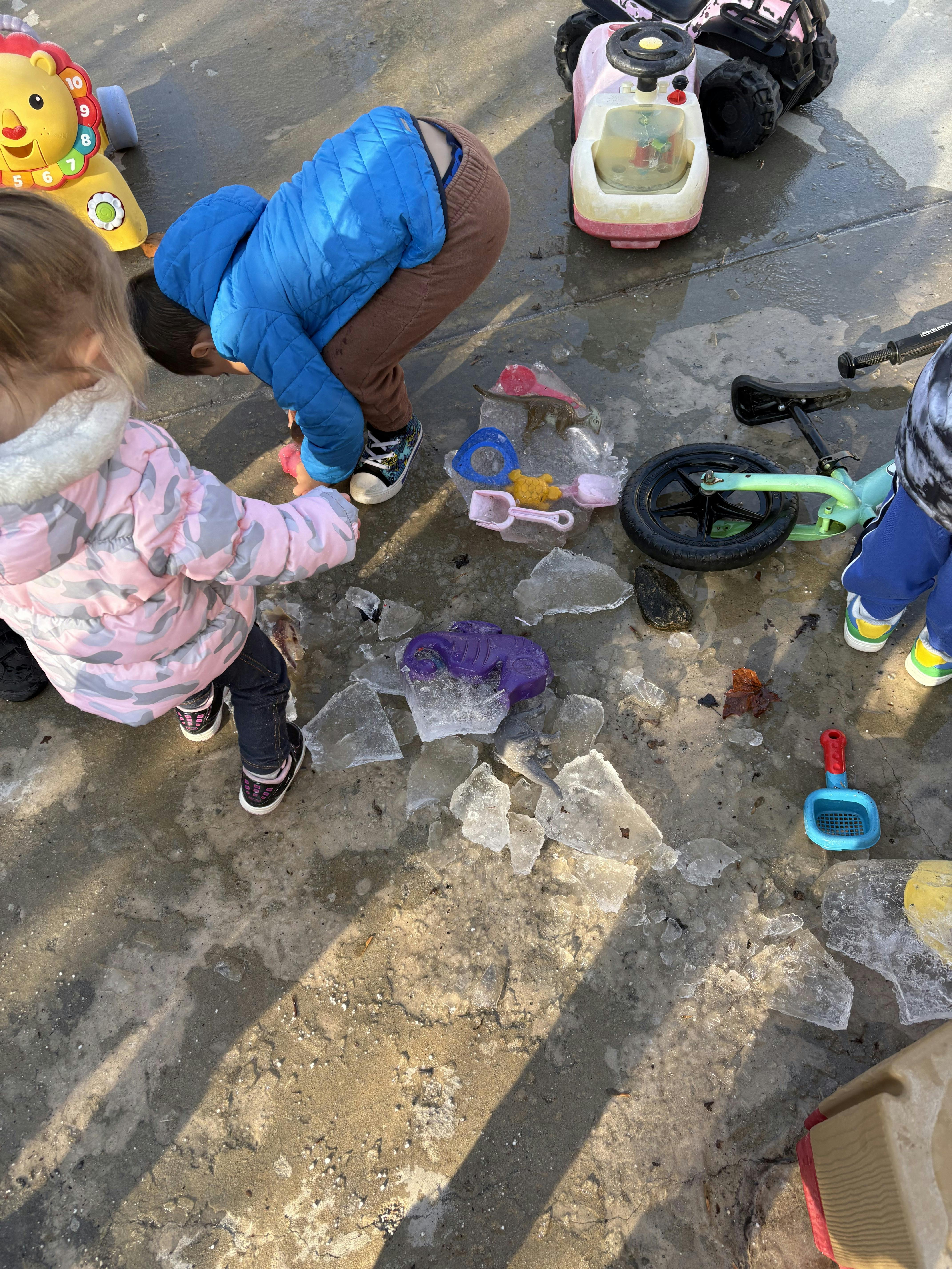 Children playing with ice and toys on a wet concrete surface
