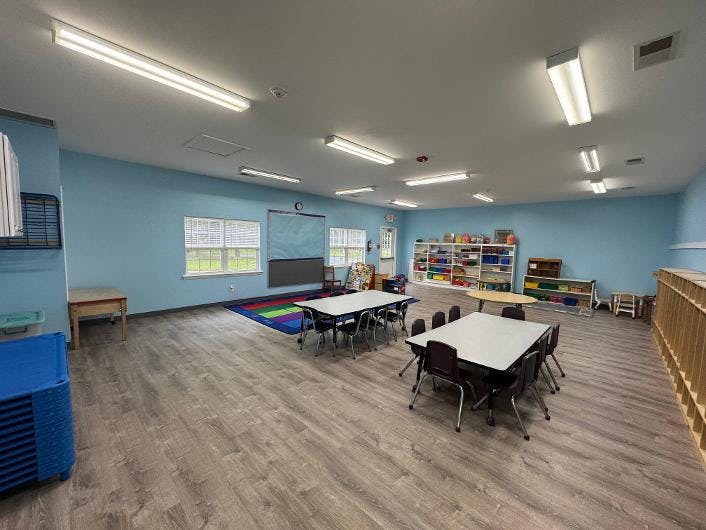 Empty preschool classroom with tables, chairs, and learning stations