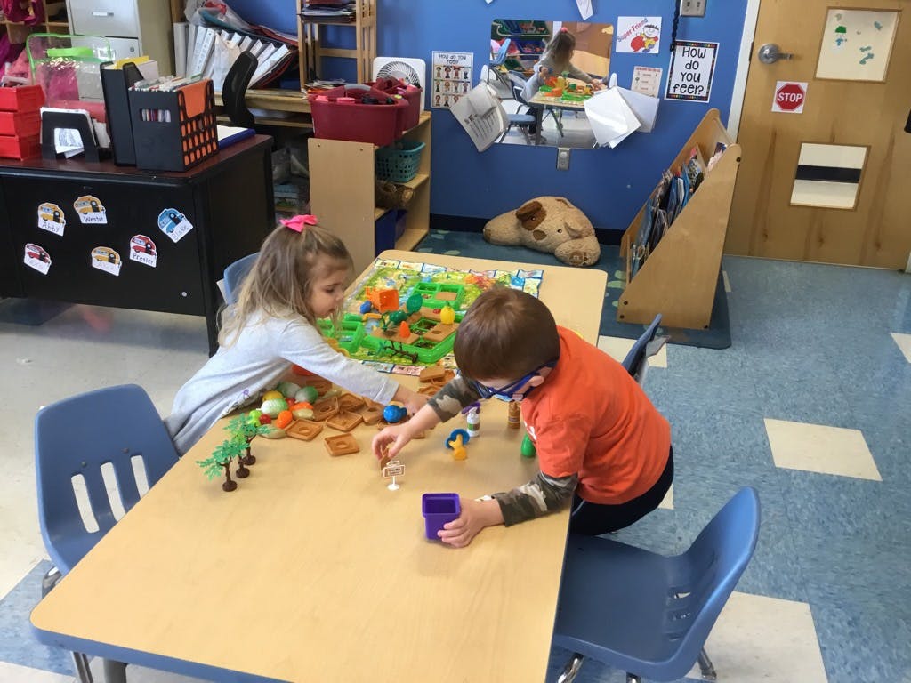 Two children playing with toys at a table in a classroom