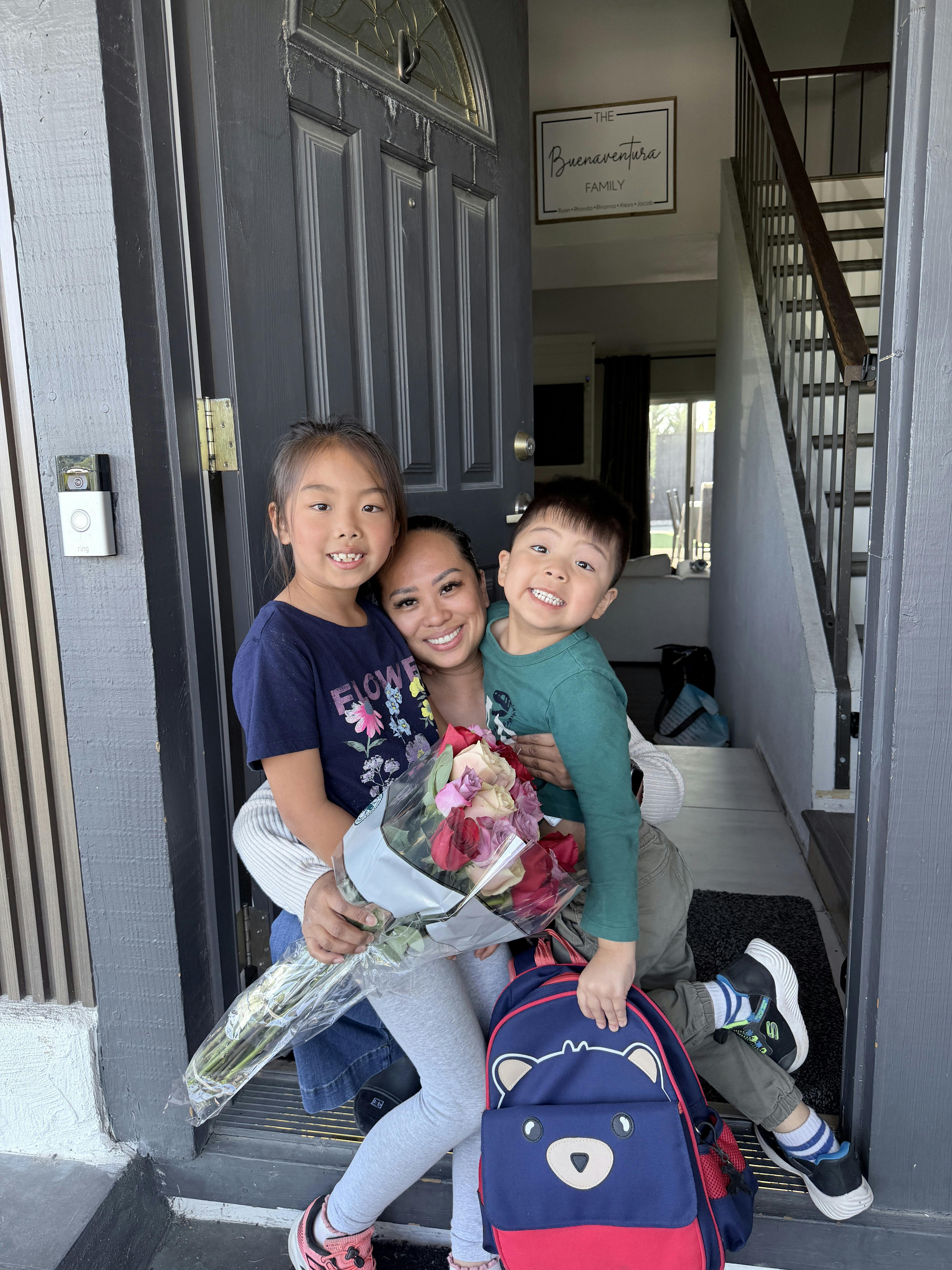 A person holding two children and a bouquet of flowers in a doorway