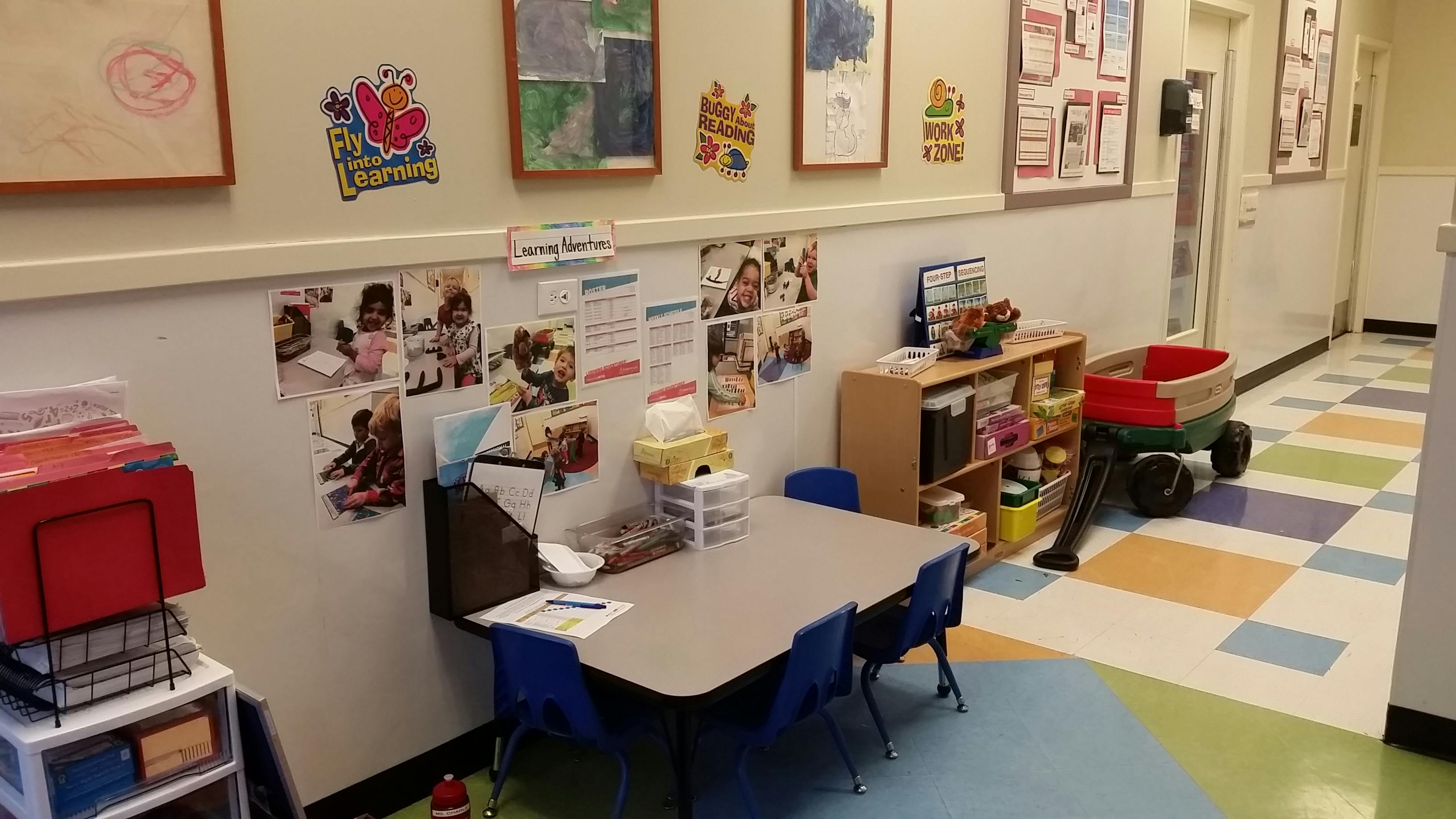 A classroom corner with a small table and chairs, and a display of children's photos