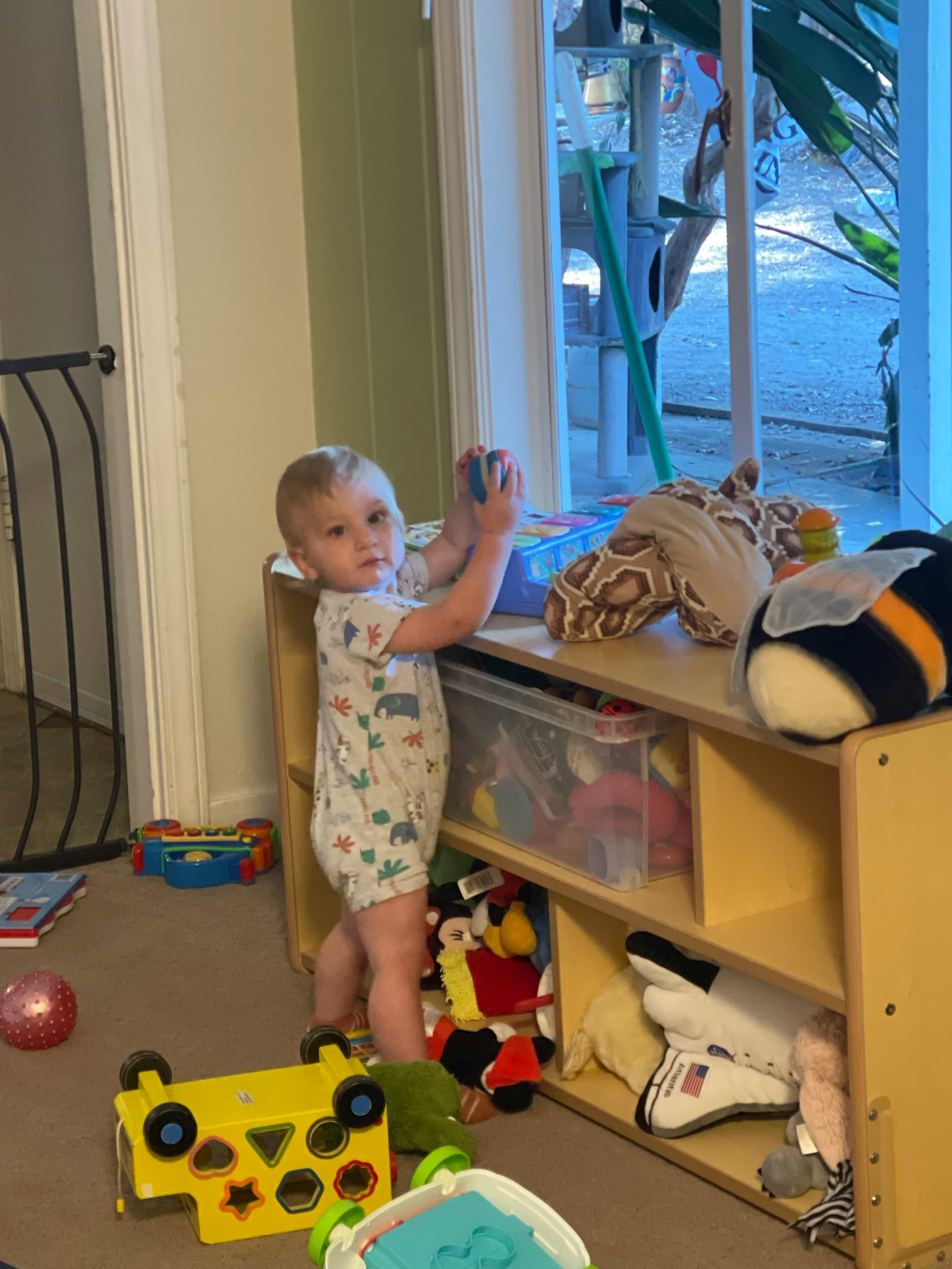 Child standing and playing with toys at a low shelf