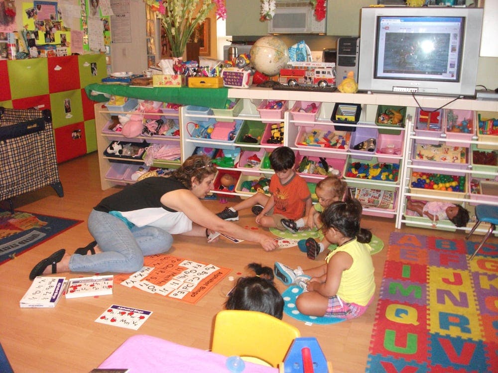 Person on floor with multiple children playing in a classroom