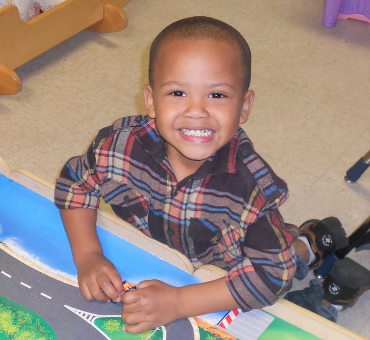 Child in plaid shirt playing with a toy car on a playmat