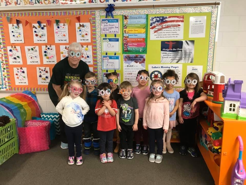 Adult and multiple children wearing paper glasses in a classroom