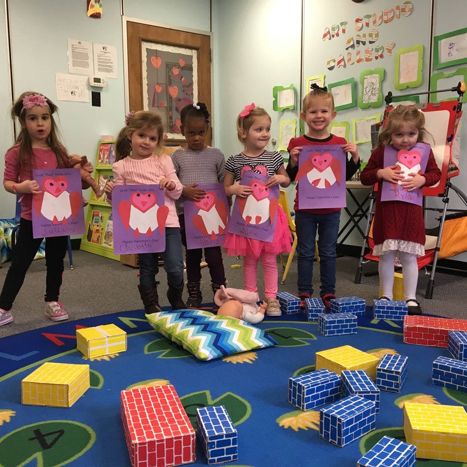 Group of children holding up paper crafts in a classroom