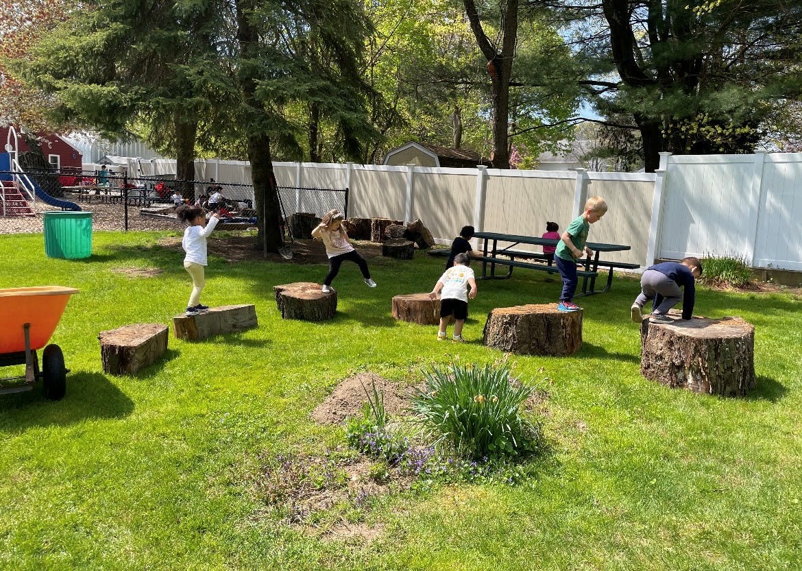 Children playing on tree stumps in a grassy outdoor area