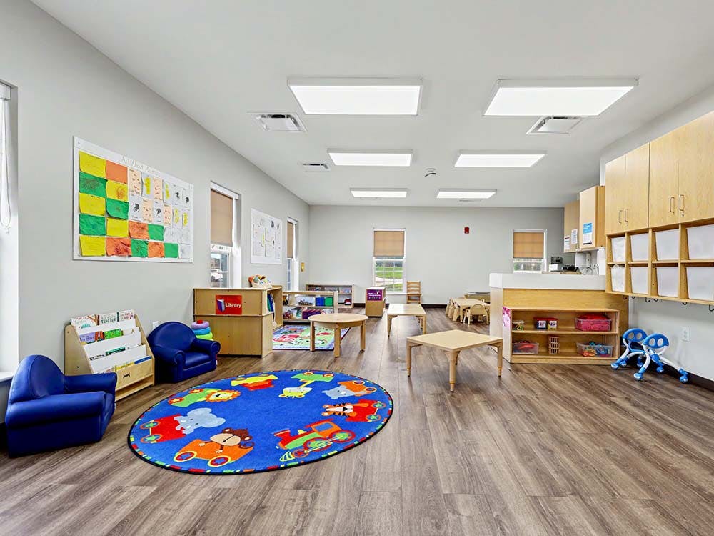 Empty classroom with small tables and chairs, a blue rug with animal patterns