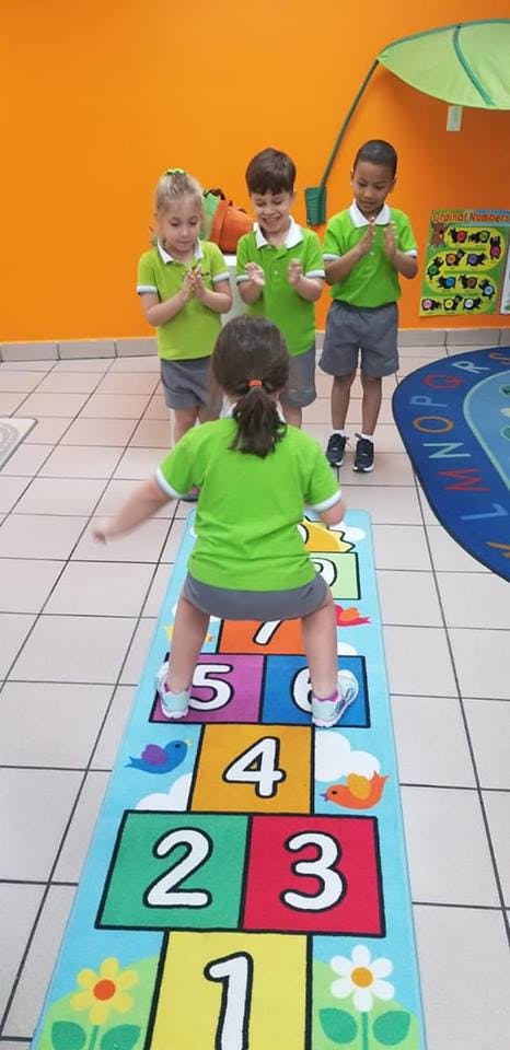 Child playing hopscotch while other children watch and an adult watch