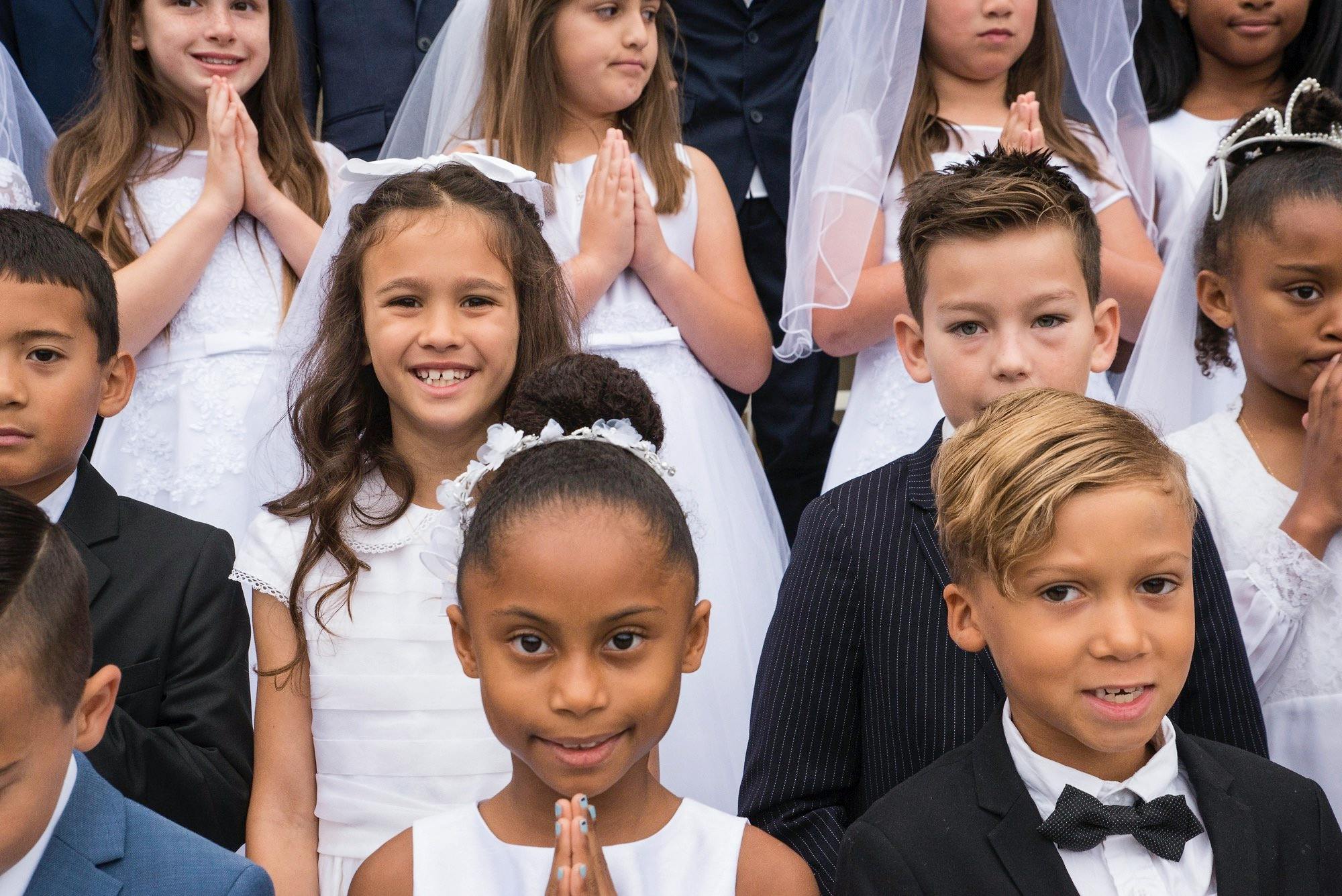 Group of children in formal attire, some with hands pressed together