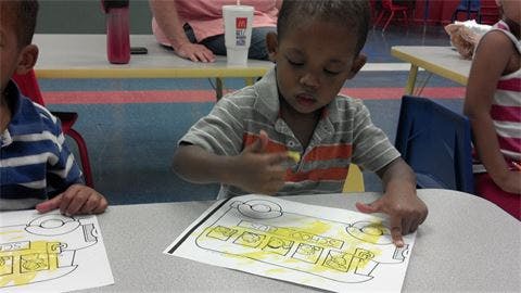 Child coloring a picture of a bus at a table