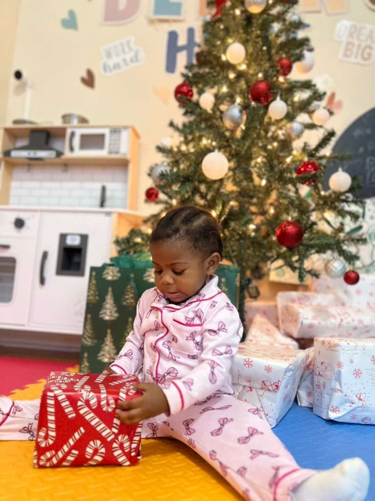 Child in pajamas opening a gift in front of a Christmas tree