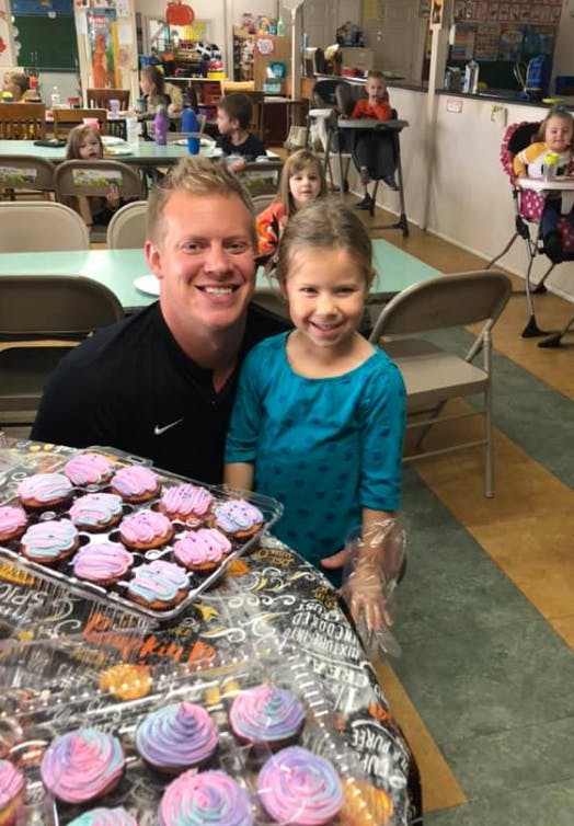 Adult and child smiling with cupcakes and cookies in a classroom