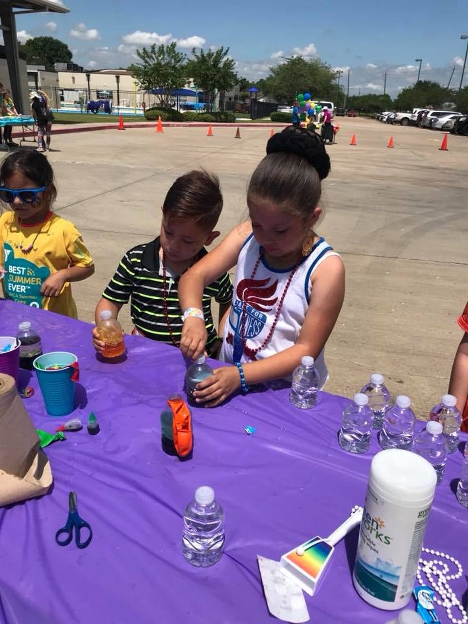Three children mixing liquids in bottles at a table