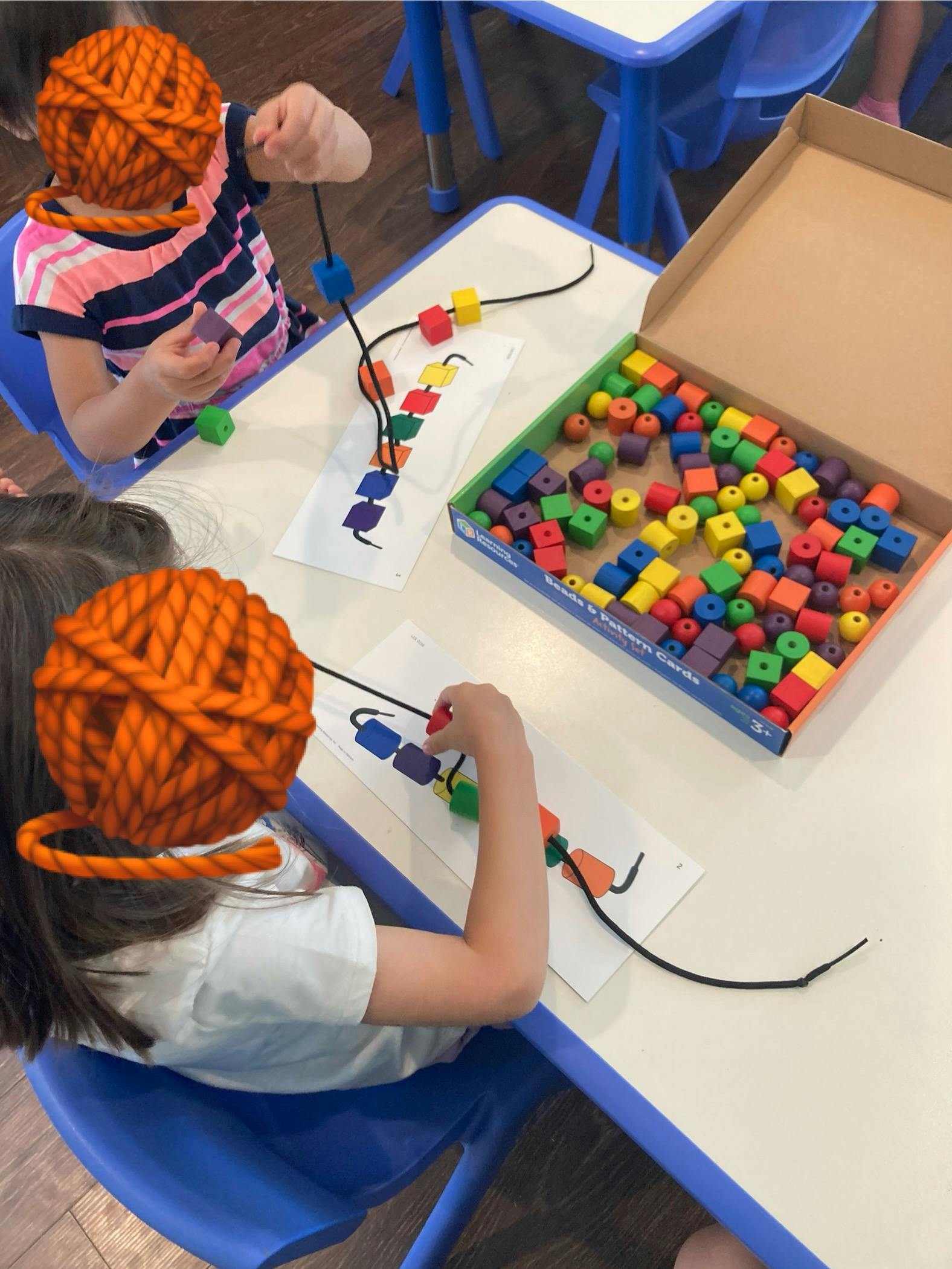 Children beading colorful blocks onto strings following pattern cards