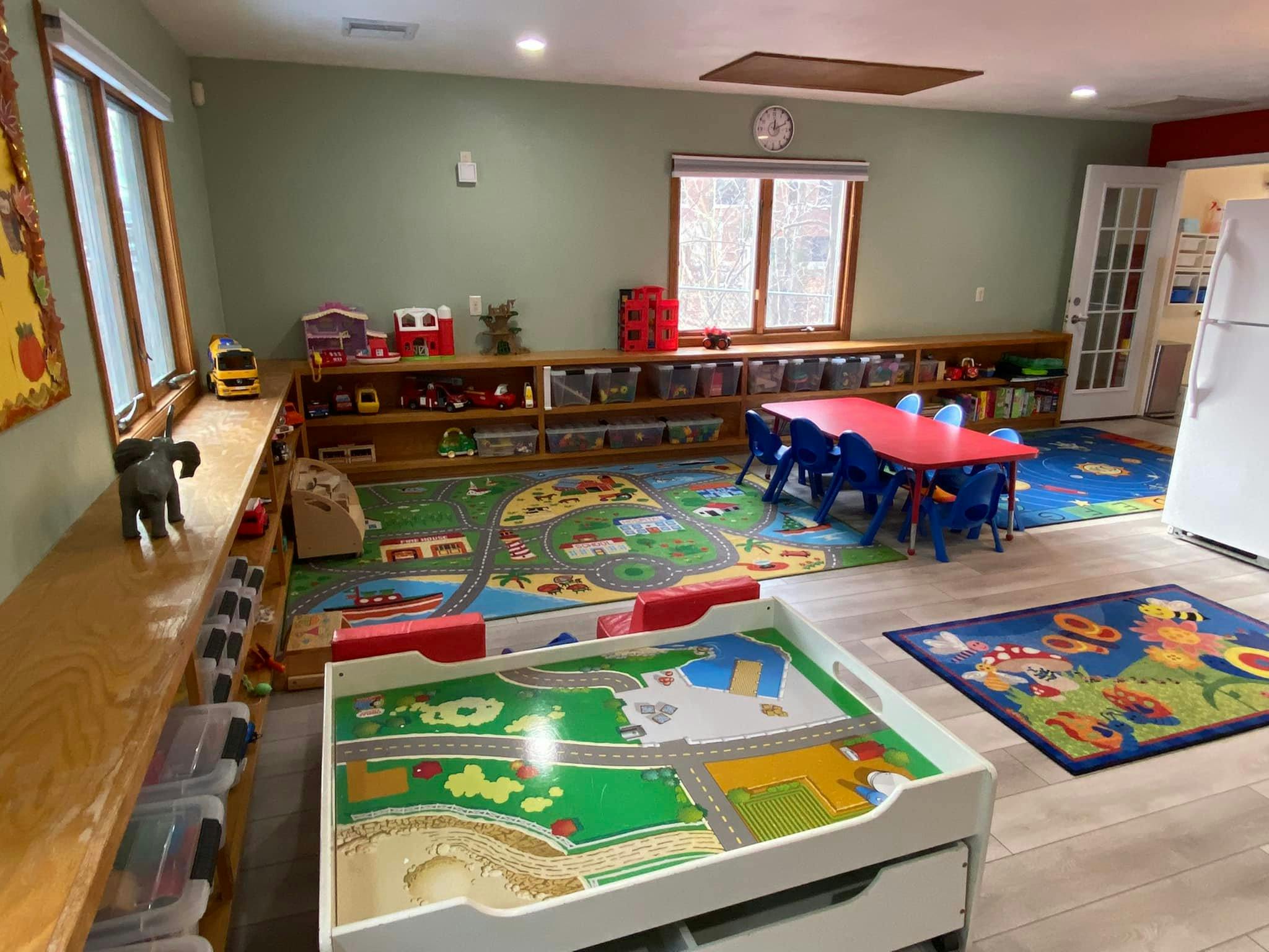 Playroom with small tables and chairs, play rugs, and shelves with toys