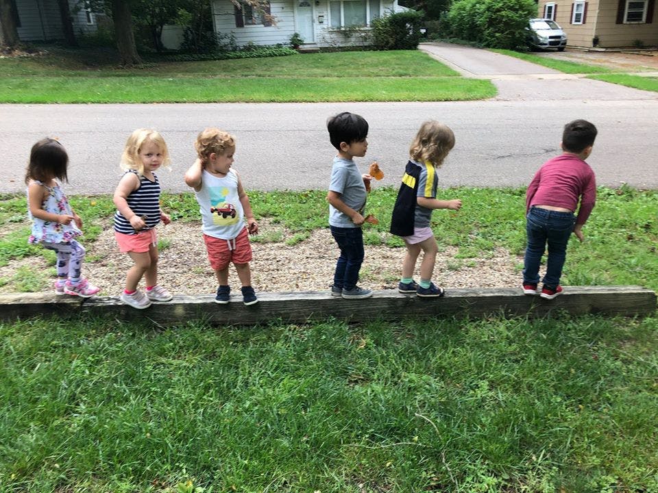 Six children walking on a wooden beam