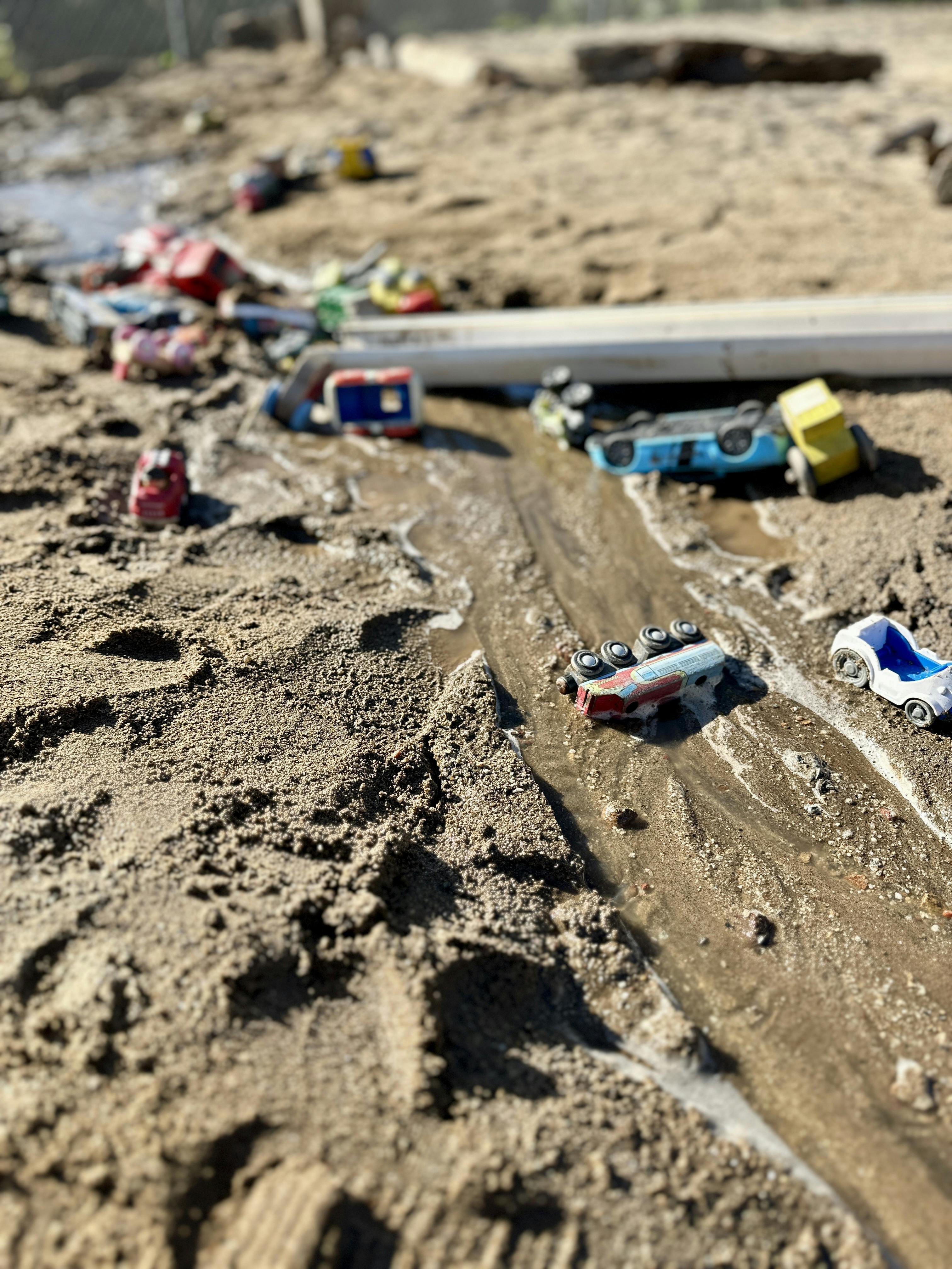 Toy cars scattered in a sandy ditch with water
