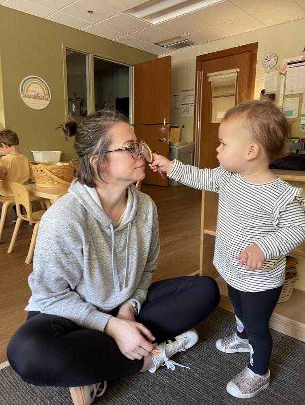 A person sitting cross-legged while a child holds a small mirror up to their nose