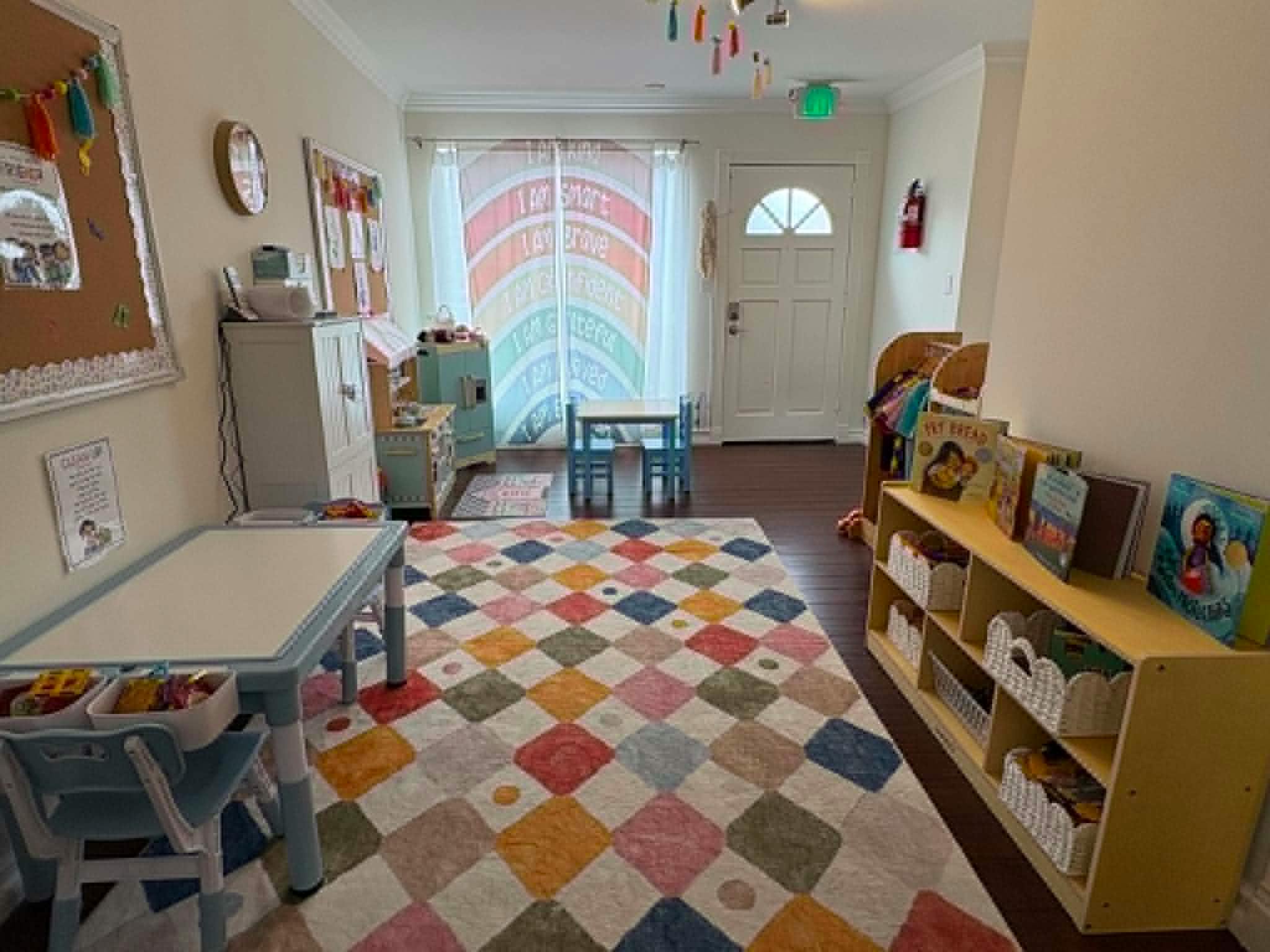 A classroom with small tables and chairs, a bookshelf, and a colorful rug