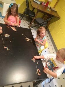 Three children making necklaces at a table