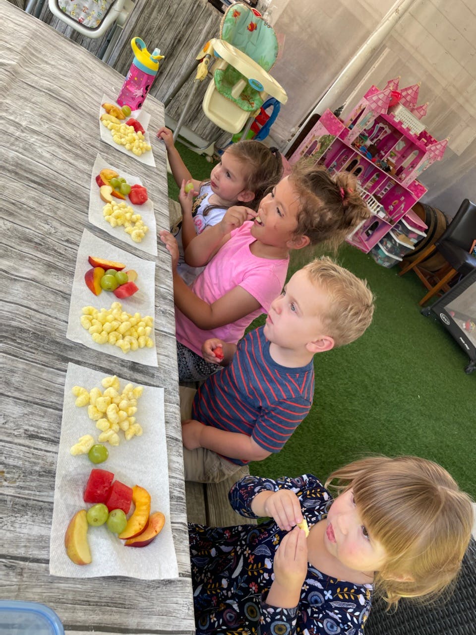 Four children eating fruit and snacks at a table