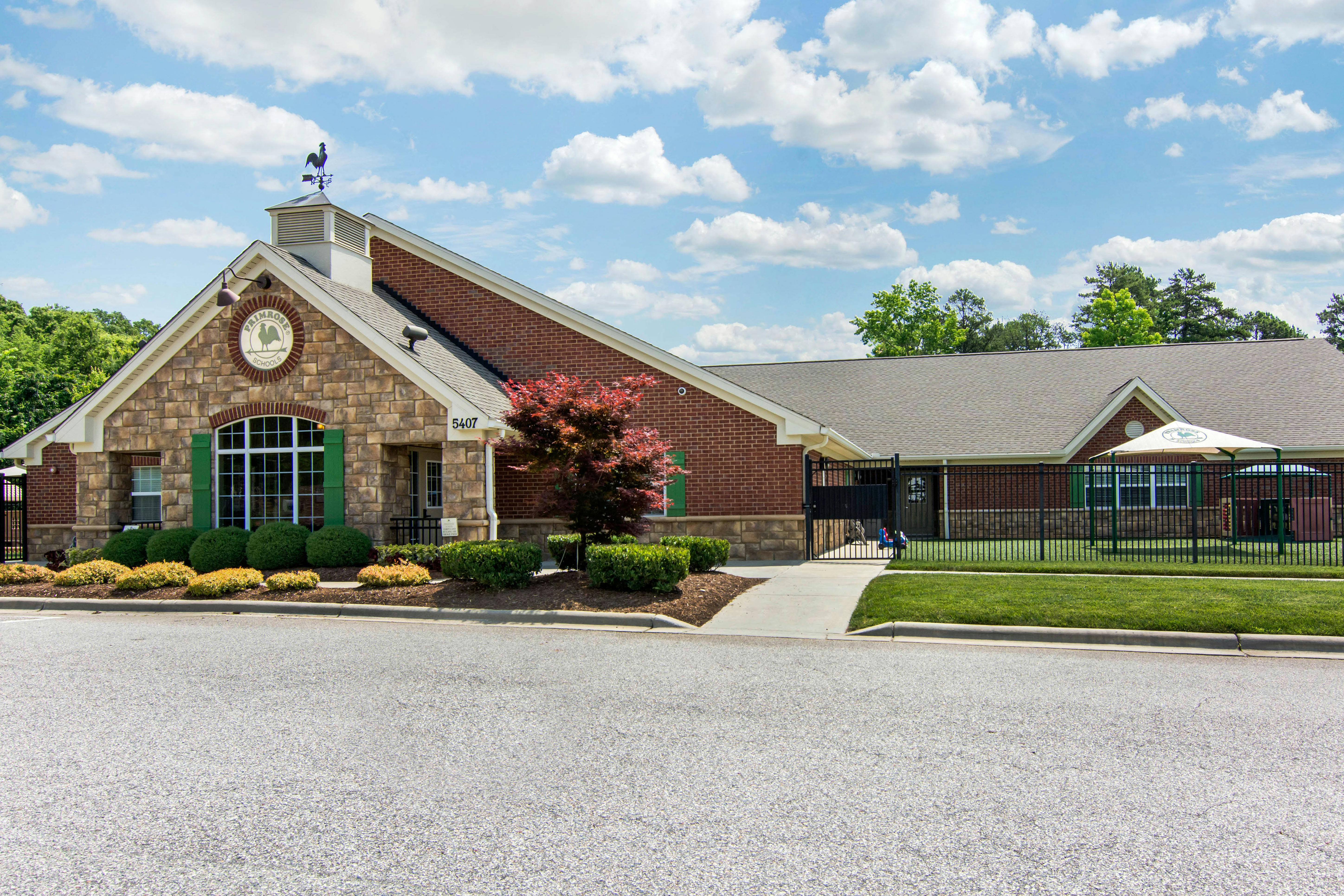 Primrose School building exterior with brick and stone, a weathervane, and green shutters