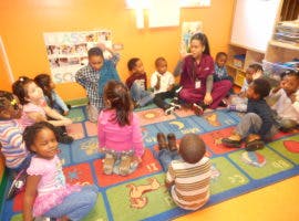 Adult and children sitting on a colorful rug in a classroom
