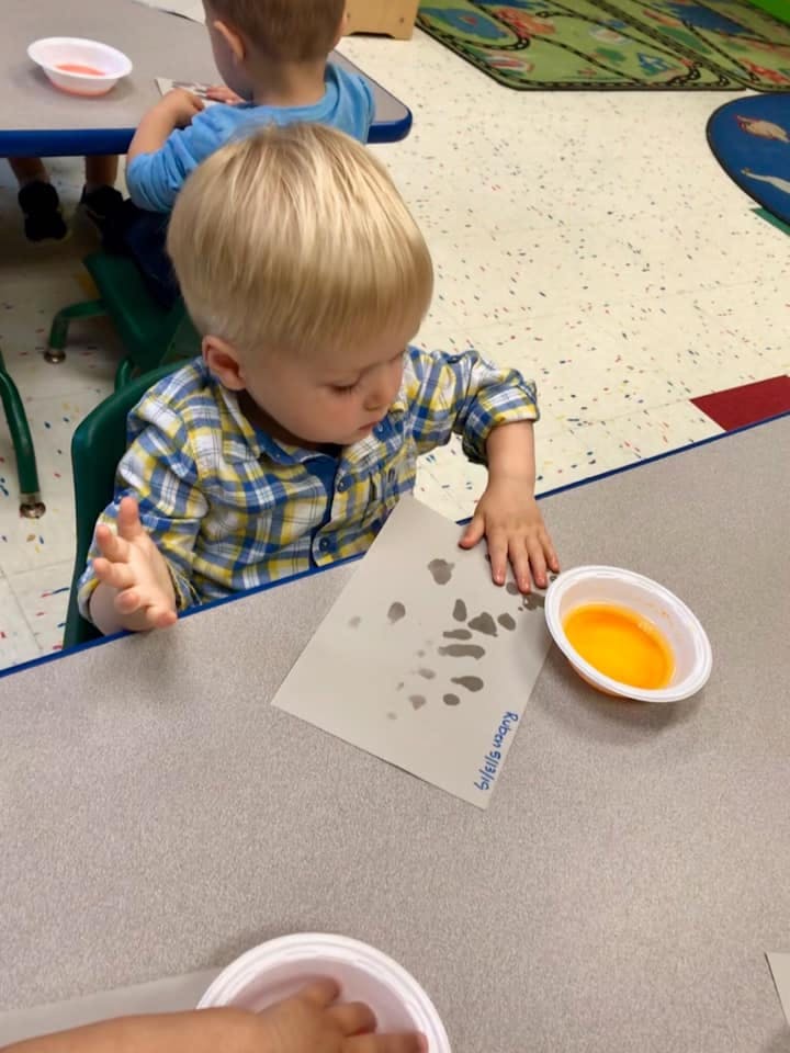 Child making handprints on paper with orange paint