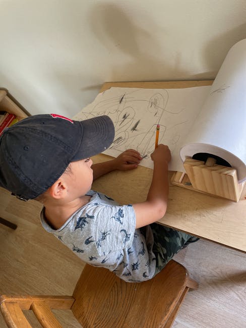 Child in a baseball cap drawing on a large paper roll with a pencil