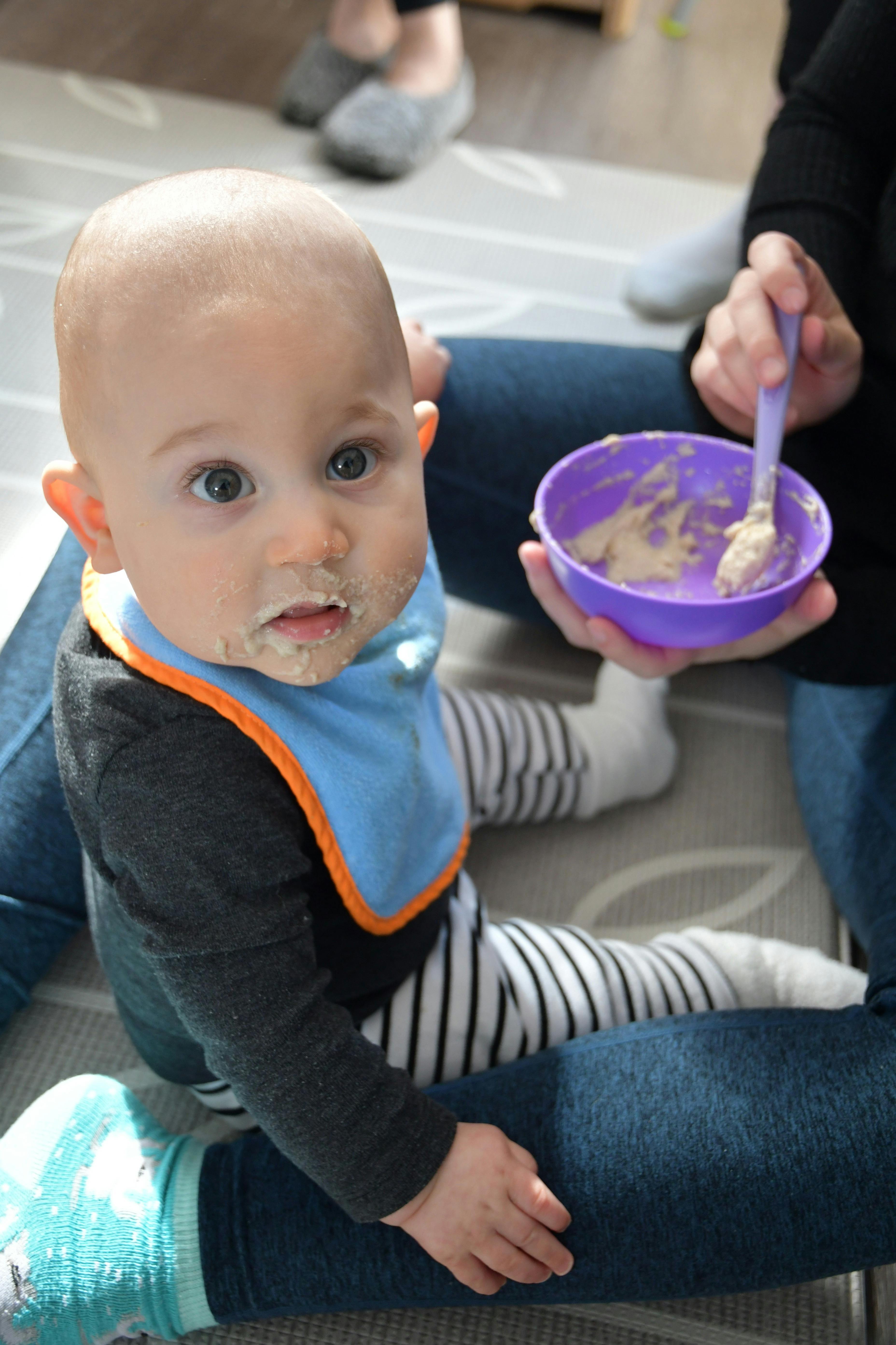 Child with food on face, person holding bowl and spoon