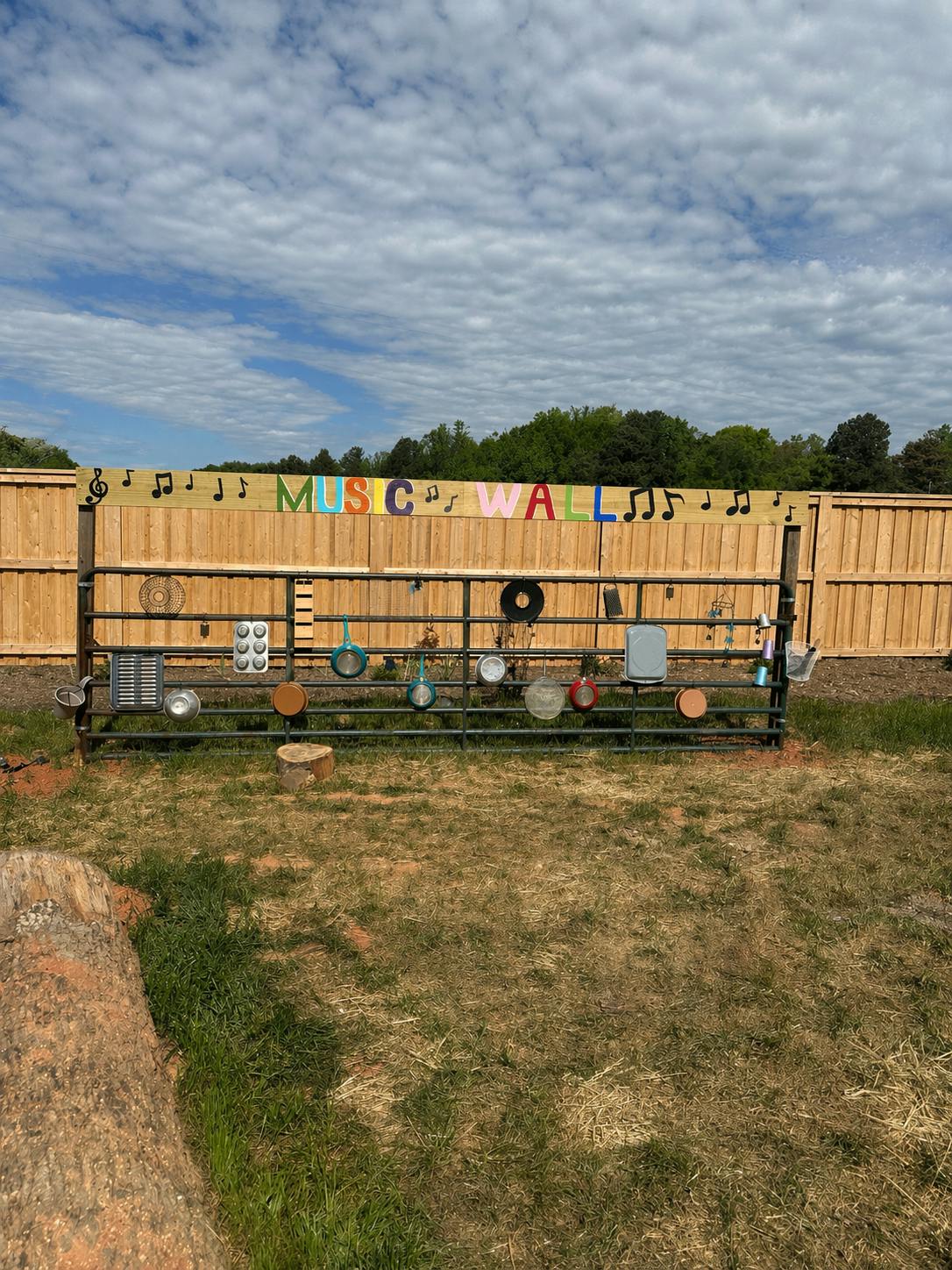 A fence with a sign that reads "MUSIC WALL" and various pots and pans hanging