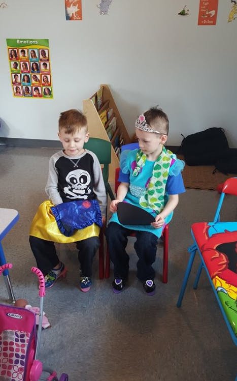 Two children sitting on chairs, one wearing a crown