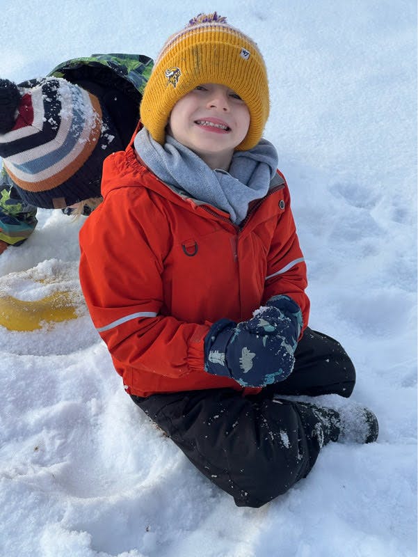 Child in orange coat, yellow hat, and mittens sitting in snow