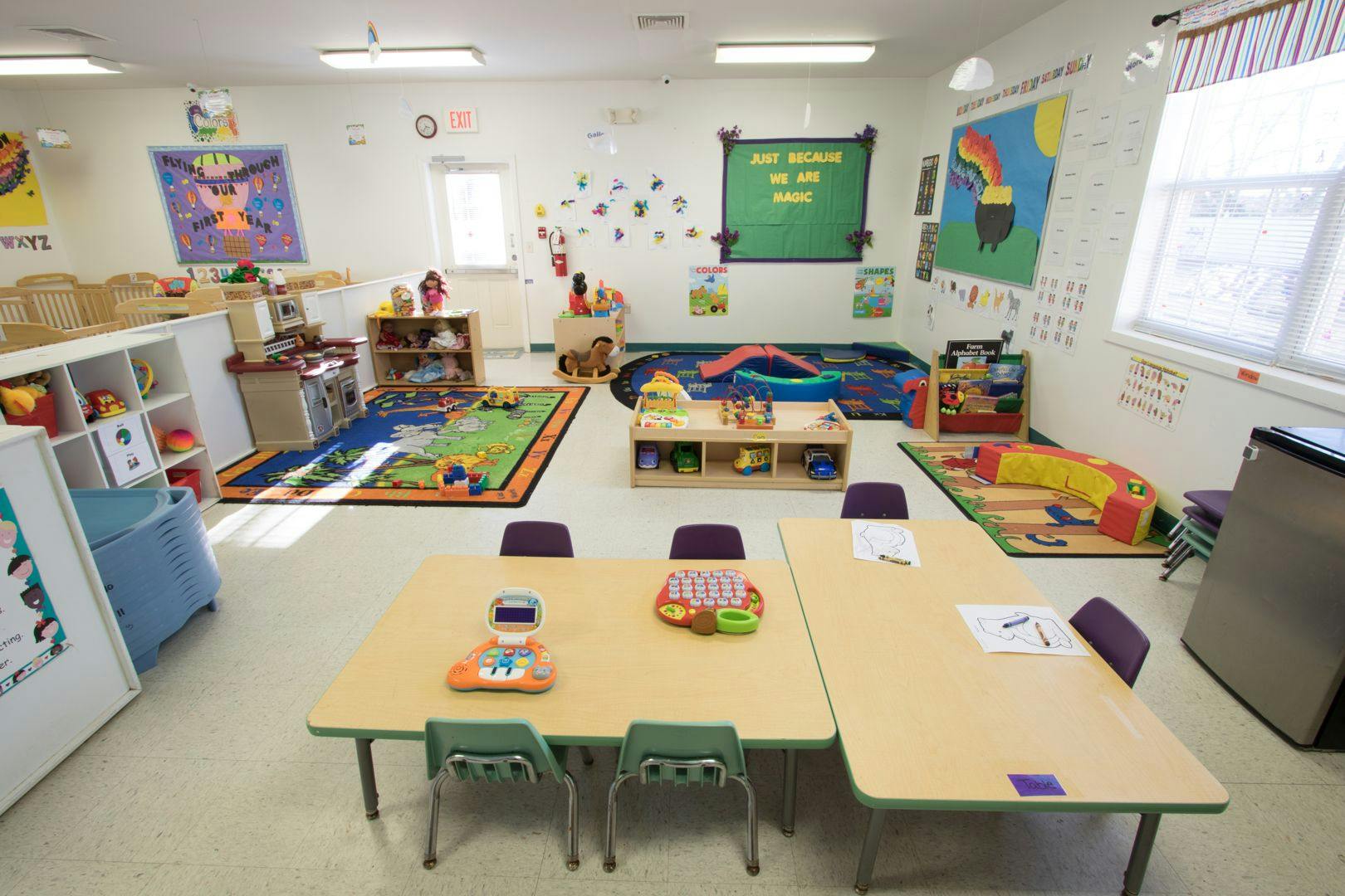 Empty classroom with small tables and chairs, rugs, and toys